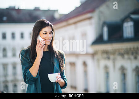 Giovane imprenditrice con lo smartphone in piedi su una terrazza al di fuori di un ufficio in città. Foto Stock