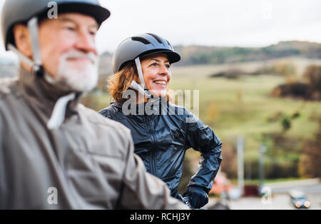 Attivo coppia senior con electrobikes in piedi all'aperto su una strada in natura. Foto Stock