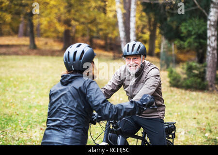 Attivo coppia senior con electrobikes in piedi all'aperto su una strada in natura. Foto Stock