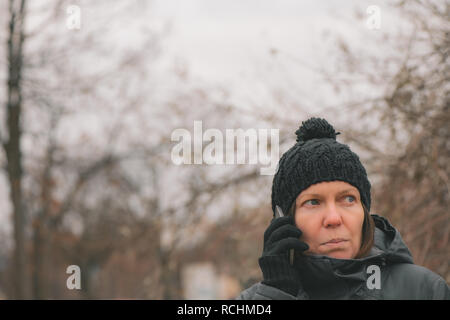 Preoccupato della donna parlando al telefono mobile su strada a freddo giorno d'inverno Foto Stock