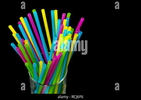 Diversi di plastica colorata cannucce potabile collocato in un bicchiere su sfondo nero.jpg Foto Stock