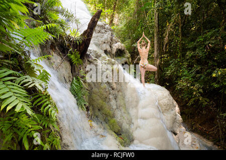 Tropical sessione di yoga da una bella cascata appiccicosa vicino a Chiang Mai nel nord della Thailandia. Vriksha asana - posizione dell'albero. Foto Stock