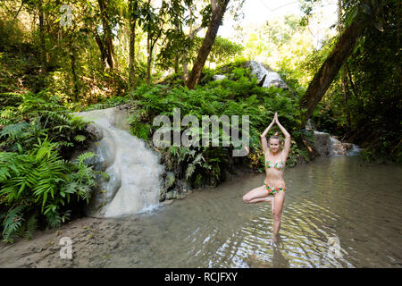 Tropical sessione di yoga da una bella cascata appiccicosa vicino a Chiang Mai nel nord della Thailandia. Vriksha asana - posizione dell'albero. Foto Stock