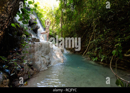 Tropical sessione di yoga da una bella cascata appiccicosa vicino a Chiang Mai nel nord della Thailandia. Vriksha asana - posizione dell'albero. Foto Stock