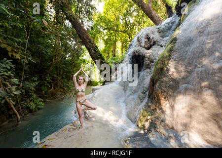 Tropical sessione di yoga da una bella cascata appiccicosa vicino a Chiang Mai nel nord della Thailandia. Vriksha asana - posizione dell'albero. Foto Stock