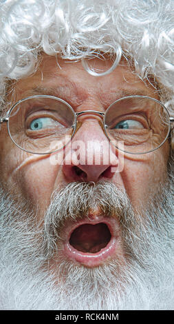 Bello il senior uomo scettico e nervoso, accigliata sconvolto a causa del problema. Persona negativa. Emozionante il volto di Babbo Natale in bicchieri. La vacanza, espressione, emozioni, senior, inverno, gesto concetto. Foto Stock