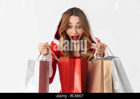 Ritratto di donna allegra 20s indossando Santa Claus costume rosso sorridente e tenendo la carta colorata borse per lo shopping con acquisti isolati su bianco bac Foto Stock