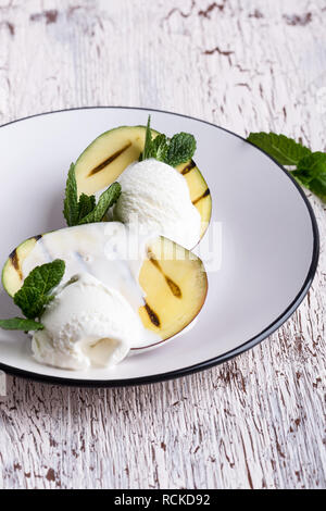 Alla griglia dessert di mango con gelato servito con foglie di menta sulla luce lastra grigia, deliziosa sorpresa vicino, il fuoco selettivo Foto Stock