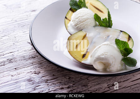 Alla griglia dessert di mango con gelato servito con foglie di menta sulla luce lastra grigia, deliziosa sorpresa vicino, il fuoco selettivo Foto Stock
