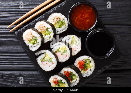 Futomaki rotoli con vari ripieni sono servite con salse close-up su una scheda di ardesia sul tavolo. parte superiore orizzontale vista da sopra Foto Stock