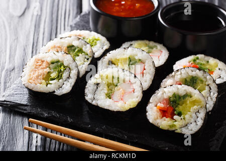 Futomaki rotoli con vari ripieni sono servite con salse close-up su una scheda di ardesia sul tavolo orizzontale. Foto Stock