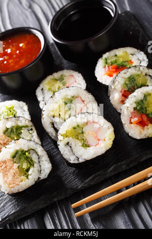 Futomaki giapponesi i rotoli con vari ripieni serviti con la soia e salse close-up su una scheda di ardesia sul piano verticale. Foto Stock