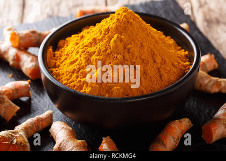 Fragranti curcuma in polvere in una ciotola e radice di close-up sul tavolo orizzontale. Foto Stock