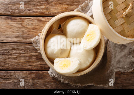 Vaporizzato Chinese bun con crema pasticcera stuff il riempimento in bamboo contenitore di legno sul tavolo. parte superiore orizzontale vista da sopra Foto Stock