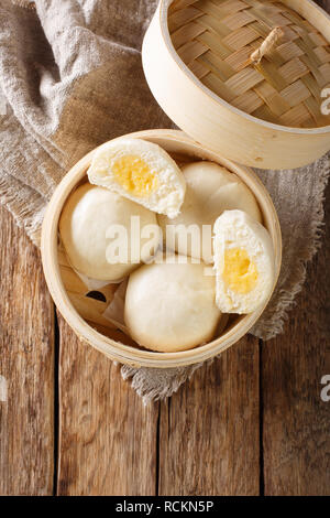 Vaporizzato Chinese bun con crema pasticcera stuff il riempimento in bamboo contenitore di legno sul tavolo. Verticale in alto vista da sopra Foto Stock