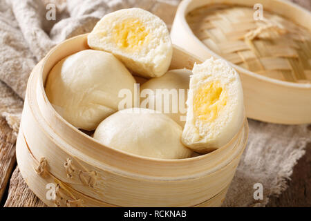 Vaporizzato Chinese bun con crema pasticcera stuff il riempimento in bamboo contenitore di legno sul tavolo orizzontale. Foto Stock