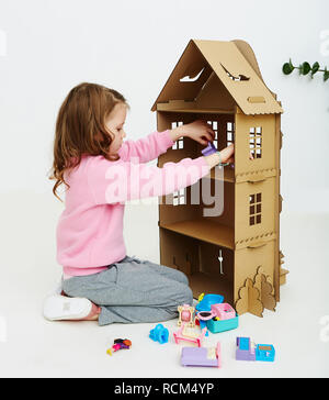 Felice bambina gioca con cartone casa di bambola. Funny bel bambino si diverte a. Foto Stock