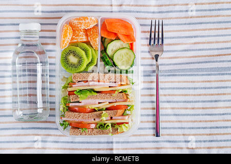 Scuola scatola di pranzo con sandwich, verdure, acqua e frutta sul tavolo. Abitudini alimentari sane concetto. Lay piatto. Vista superiore Foto Stock