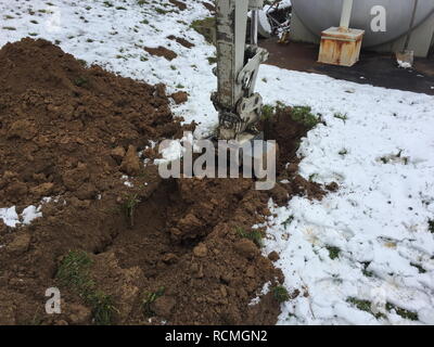 Escavatore pala scava in un suolo coperto di neve. Foto Stock
