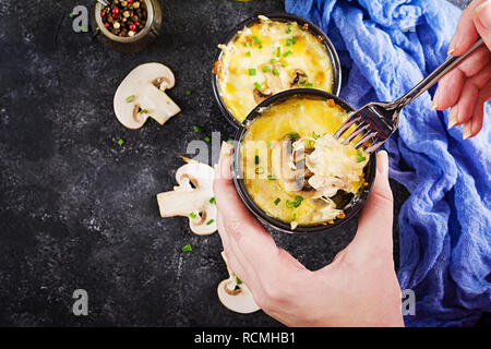 Funghi cotti al forno con julienne di pollo e formaggio in pentole. Vista dall'alto. Pentola con una julienne in mani Foto Stock