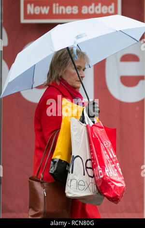 Negozi, shipper, shopping in una giornata bagnata inPreston, Lancashire, gennaio 2019. Meteo Regno Unito. Il bagnata e ventosa inizia la giornata nel centro della città. La pioggia si muove verso est attraverso l'Inghilterra con forti docce a nord e ovest, girando sempre più vino. Donna che passa la finestra di vendita che trasporta i sacchetti di shopping di vendita seguente. Sconti, vendita, sdoganamento, moda, vendita di abbigliamento. Foto Stock