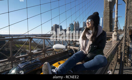 Giovani e spericolate ragazza si siede sul bordo del ponte di Brooklyn a New York Foto Stock