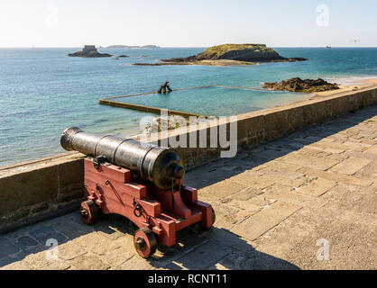 La marea piscina di Saint-Malo, Francia, al tramonto con un vecchio cannone in primo piano e il Grand e Petit essere isole nella distanza. Foto Stock