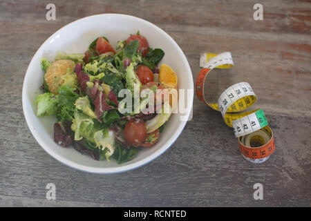 Miscelati verde e viola insalata con nastro di misurazione sul malandato brown tavolo in legno diete fitness salute sfondo concettuale. Foto Stock