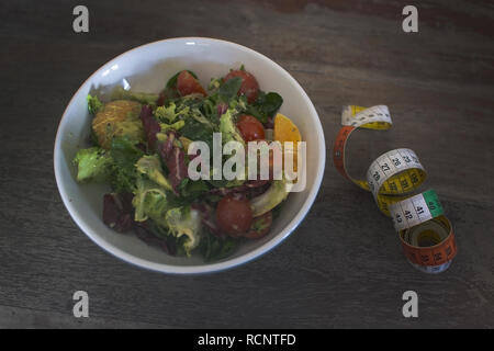 Miscelati verde e viola insalata con nastro di misurazione sul malandato brown tavolo in legno diete fitness salute sfondo concettuale. Foto Stock