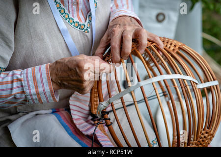 Vecchia donna in costume nazionale rendi locale cesto in vimini. Artigianato tradizionale concetto. Lettonia - Immagine Foto Stock