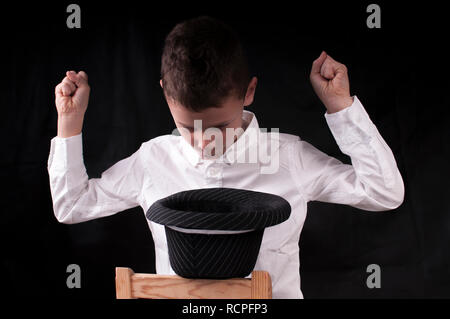 Ragazzo in una camicia bianca su sfondo nero evoca da un cappello Foto Stock