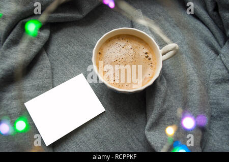 Weekend caldo in condizioni climatiche fredde. Una tazza di caffè sul tessile uno sfondo grigio con una ghirlanda e copyspace. Foto Stock