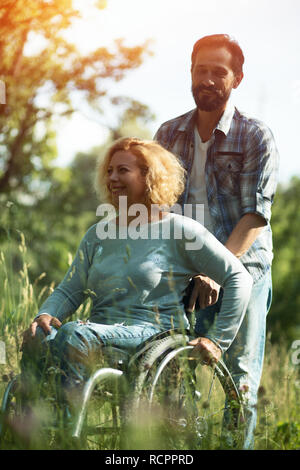 Donna felice in carrozzina con il marito. All'aperto Foto Stock