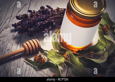 Il miele in barattolo con miele bilanciere e lavanda e i fiori di tiglio su vintage sfondo di legno. Foto Stock