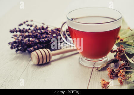 Tazza di tè con miele bilanciere e lavanda e i fiori di tiglio su vintage sfondo di legno. Foto Stock
