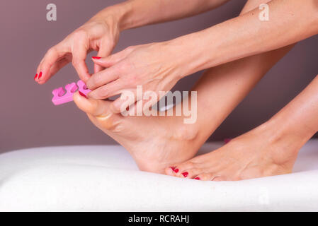 Applicazione di pedicure per donna di piedi con red toenails, nella rosa dei separatori di convergenza . Foto Stock