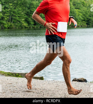 Babilonia, New York, Stati Uniti d'America - 12 August 2018: un runner è in esecuzione un 10.000 metri di gara con nessuno scarpe on, off road nelle prove passando un lago durante il Di Foto Stock