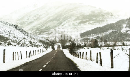 Inverno strada innevata in una foresta senza automobili, portando in montagna. Laciana, Leon, Spagna. Foto Stock