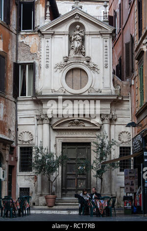 Giovane si siede a un cafe' all'aperto a Roma vicino la facciata barocca della chiesa di Santa Barbara dei Librai nel rione Parione. Foto Stock