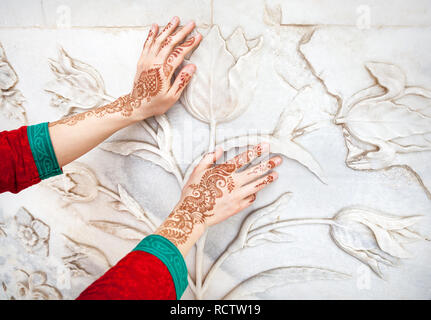 Woman in Red costume indiano toccando il marmo bianco parete con motivo floreale dalle mani di pittura henné in Taj Mahal di Agra, Uttar Pradesh, India Foto Stock