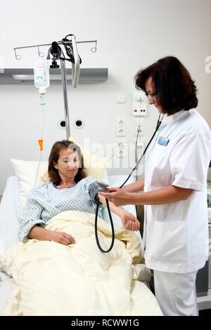 L'infermiera controllando la pressione del sangue di un paziente che si trova in un letto di ospedale, ospedale Foto Stock