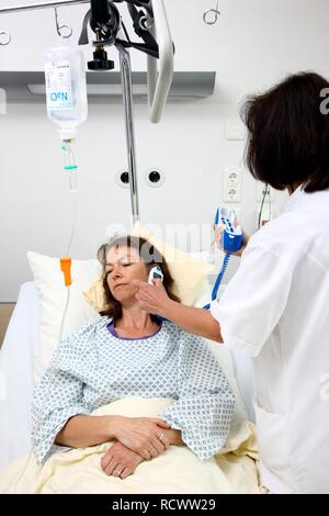 L'infermiera usando un termometro digitale per misurare la temperatura del corpo di un paziente in un letto di ospedale Foto Stock