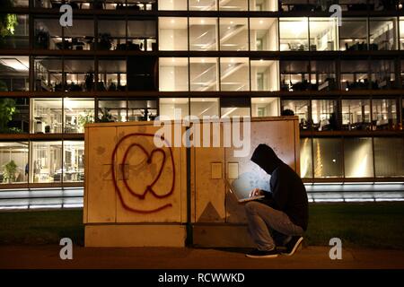 Hacker che lavora su un computer portatile davanti a un edificio commerciale, la pirateria in rete della società, immagine simbolica per Foto Stock