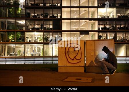 Hacker che lavora su un computer portatile davanti a un edificio commerciale, la pirateria in rete della società, immagine simbolica per Foto Stock