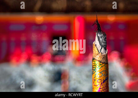 Una fumante joss aroma bastoncini di incenso o candela nel turibolo contro lo sfondo sfocato all'ingresso di un tempio buddista. Foto Stock