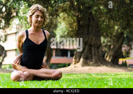 Bella donna a praticare yoga nel parco.La bloccato Lotus pongono Baddha Padmasana Foto Stock