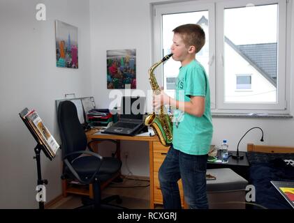 Il ragazzo, 12 anni, praticando il sassofono nella sua stanza Foto Stock