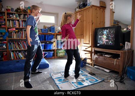 Fratelli, un ragazzo, 12 anni, e una ragazza di 10 anni, la riproduzione di un gioco di ballo su un Wii console giochi nel loro insieme in camera Foto Stock