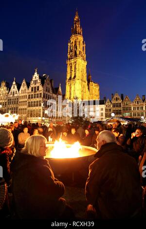 Persone bevendo un vin brulé attorno ad una grande fiamma a gas falò, mercatino di Natale presso il municipio sul Grote Markt Foto Stock