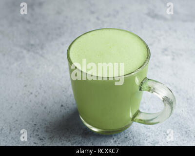 Bevanda alla moda idea: tè verde Matcha latte nella tazza di vetro. Matcha latte su sfondo grigio. Copia dello spazio. Foto Stock